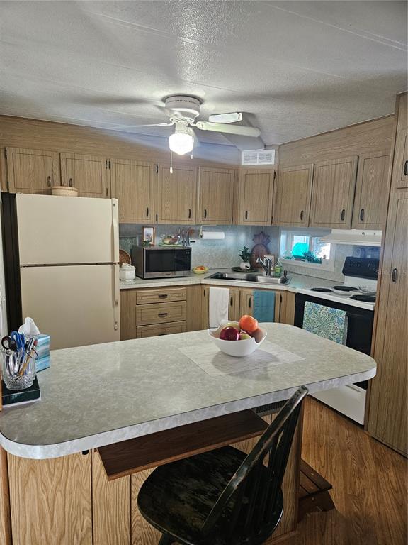 A kitchen features wood cabinets, a central island, and white appliances — 5670 TEAHOUSE ROAD, VENICE, FL