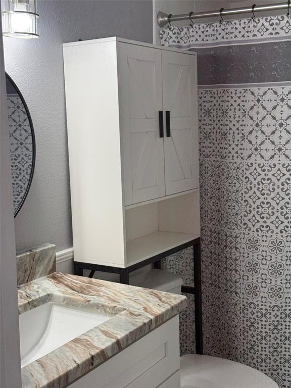 A bathroom features a white over-the-toilet storage cabinet, a marble vanity, and a patterned shower curtain — 1000 APOLLO BEACH BOULEVARD UNIT 204, APOLLO BEACH, FL