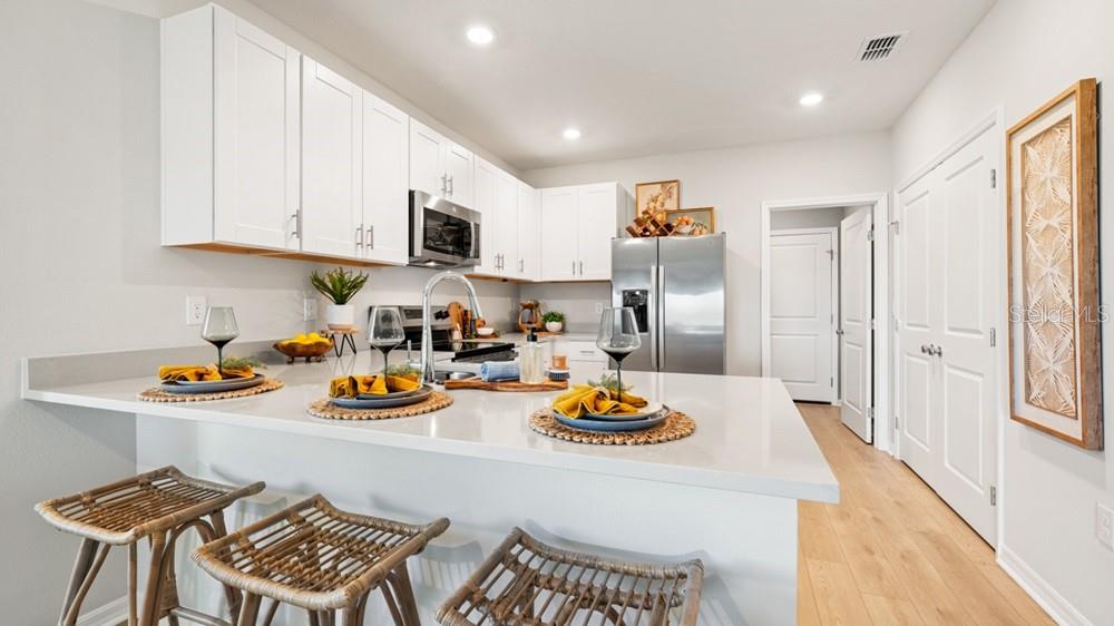 A modern kitchen features white cabinets, stainless steel appliances, and a quartz breakfast bar — 13512 SAWMILL STREET, PARRISH, FL