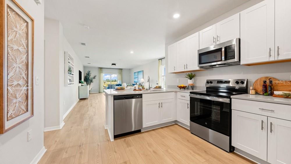 A modern kitchen with white cabinets, stainless steel appliances, and light wood flooring — 13512 SAWMILL STREET, PARRISH, FL