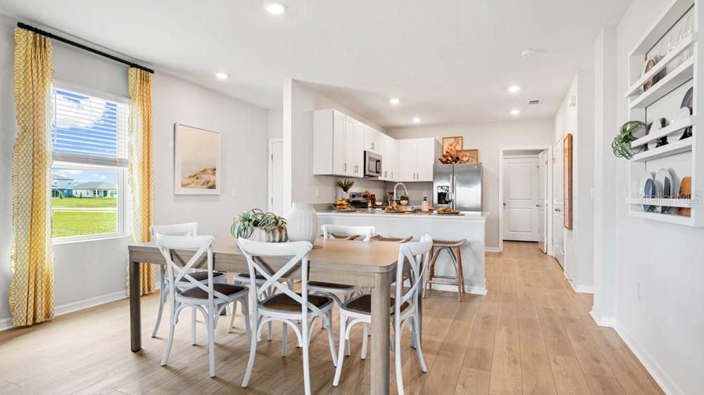 A dining area with a wooden table and white chairs sits before an open kitchen — 13512 SAWMILL STREET, PARRISH, FL