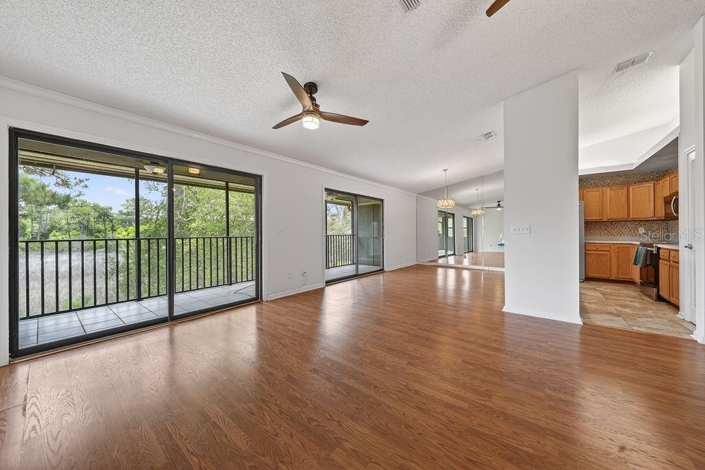 A living room with wood-look flooring, a ceiling fan, sliding glass doors, and an adjacent kitchen — 18 TALAVERA COURT UNIT 18, ST AUGUSTINE, FL