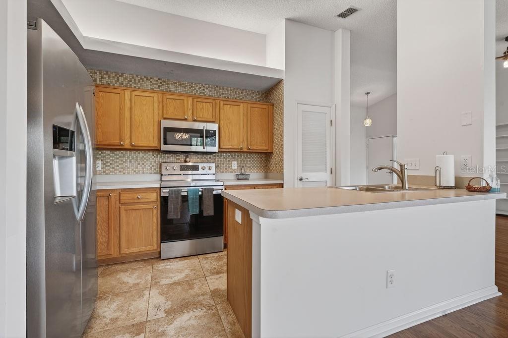 A kitchen features wood cabinets, stainless steel appliances, a tiled backsplash, and a breakfast bar — 18 TALAVERA COURT UNIT 18, ST AUGUSTINE, FL