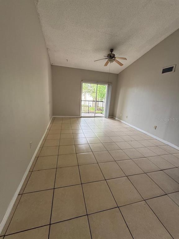 An empty living room features beige tile flooring, a vaulted ceiling with a fan, and sliding doors — 1956 LAKE ATRIUMS CIRCLE UNIT 150, ORLANDO, FL