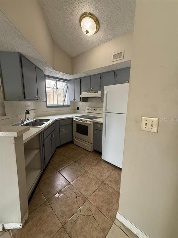 A kitchen features gray cabinets, white appliances, a double sink, and cracked tile flooring — 1956 LAKE ATRIUMS CIRCLE UNIT 150, ORLANDO, FL