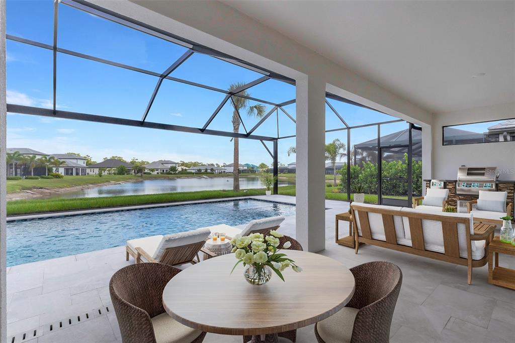 A covered patio features a swimming pool, outdoor kitchen, and dining area overlooking a lake — 1669 LUGANO CIRCLE, NOKOMIS, FL