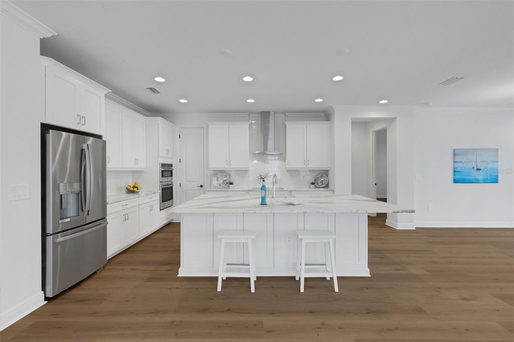 A modern kitchen features white cabinetry, a large marble-topped island, and stainless steel appliances — 1669 LUGANO CIRCLE, NOKOMIS, FL