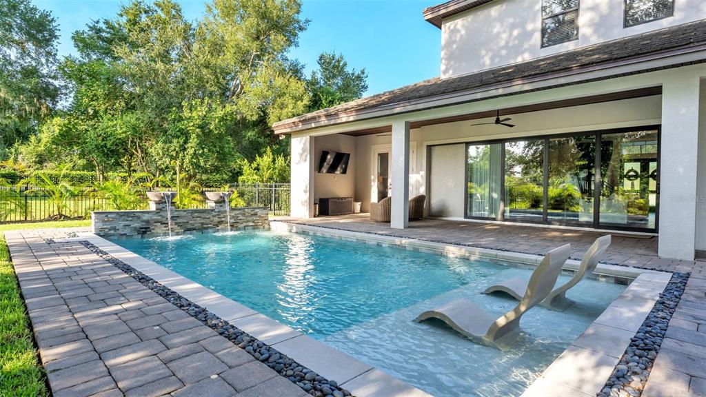 A backyard swimming pool with a sun shelf, water features, and a covered patio area — 2476 DELPHI CIRCLE, LAKELAND, FL