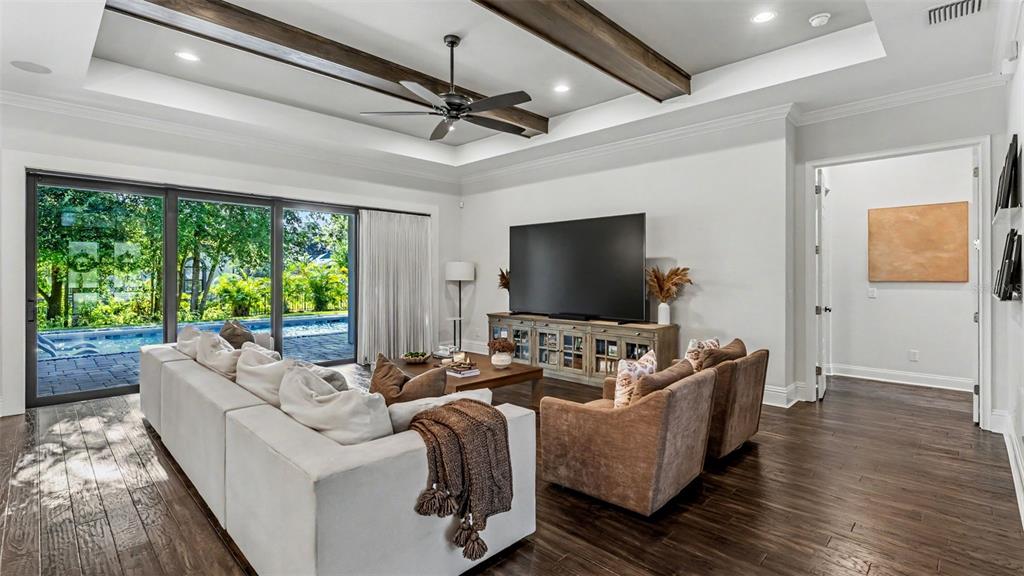 A living room features a white sectional, brown armchairs, wood ceiling beams, and sliding glass doors — 2476 DELPHI CIRCLE, LAKELAND, FL