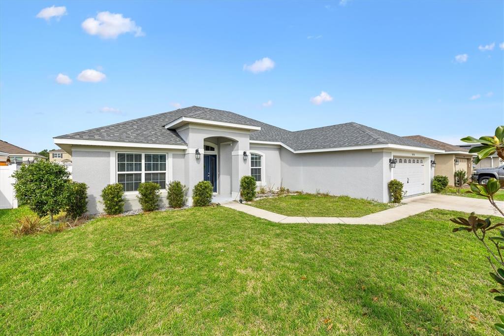 A single-story house with a gray stucco exterior, a shingled roof, and a front lawn — 9778 PEPPER TREE PLACE, WILDWOOD, FL