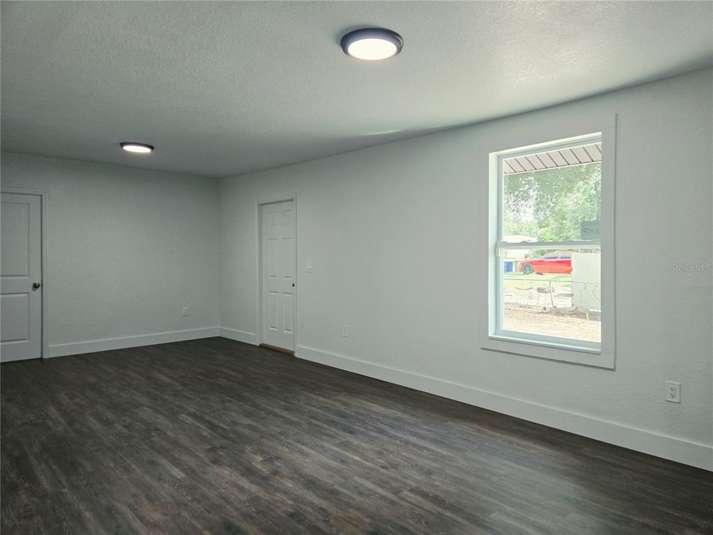 An empty room features white walls, dark wood-look flooring, two ceiling lights, and a window — 9408 N 12TH STREET, TAMPA, FL