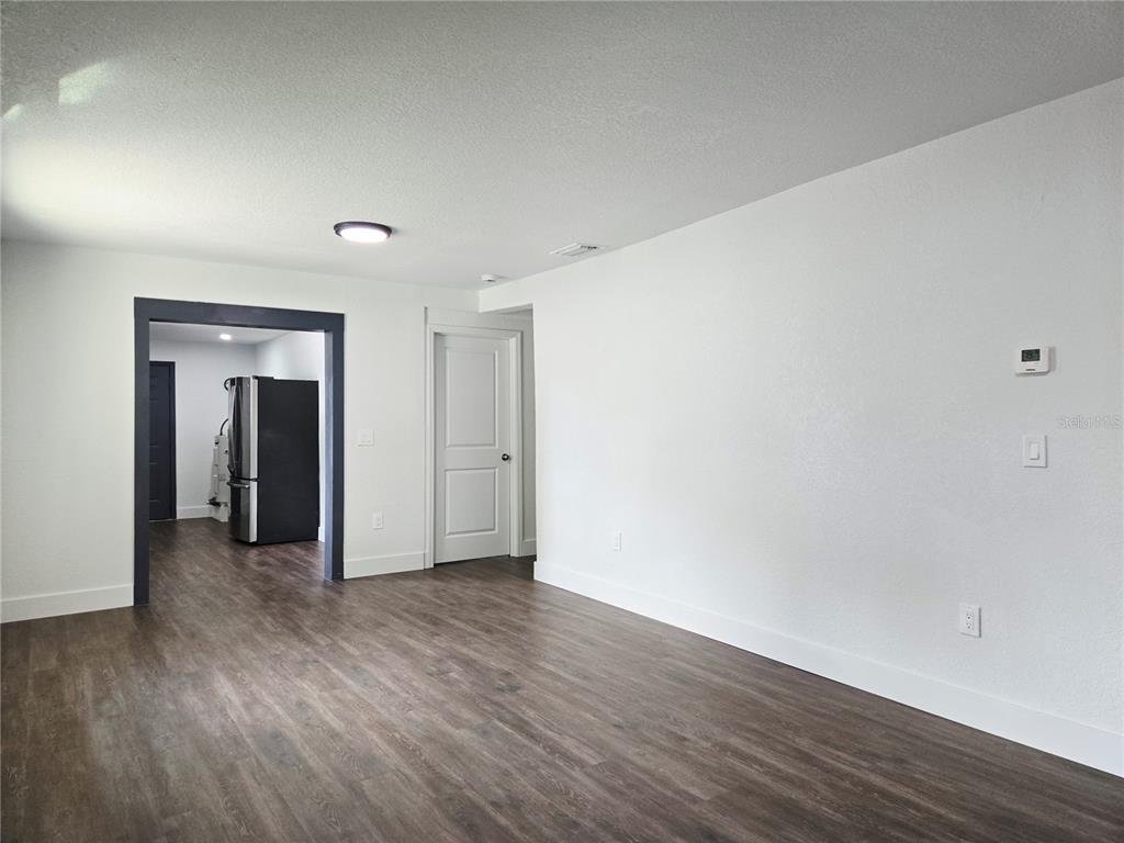 An empty room features white walls, dark wood-look flooring, a doorway to a kitchen, and a closet — 9408 N 12TH STREET, TAMPA, FL