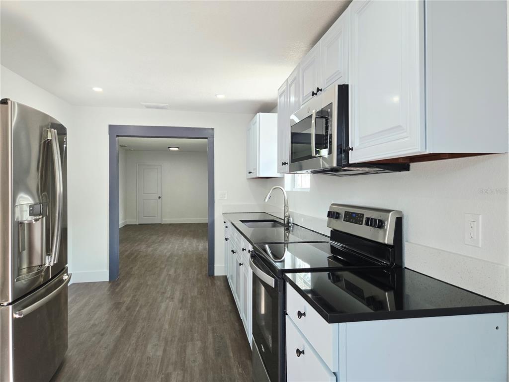 A kitchen with white cabinets, black countertops, stainless steel appliances, and wood-look flooring — 9408 N 12TH STREET, TAMPA, FL