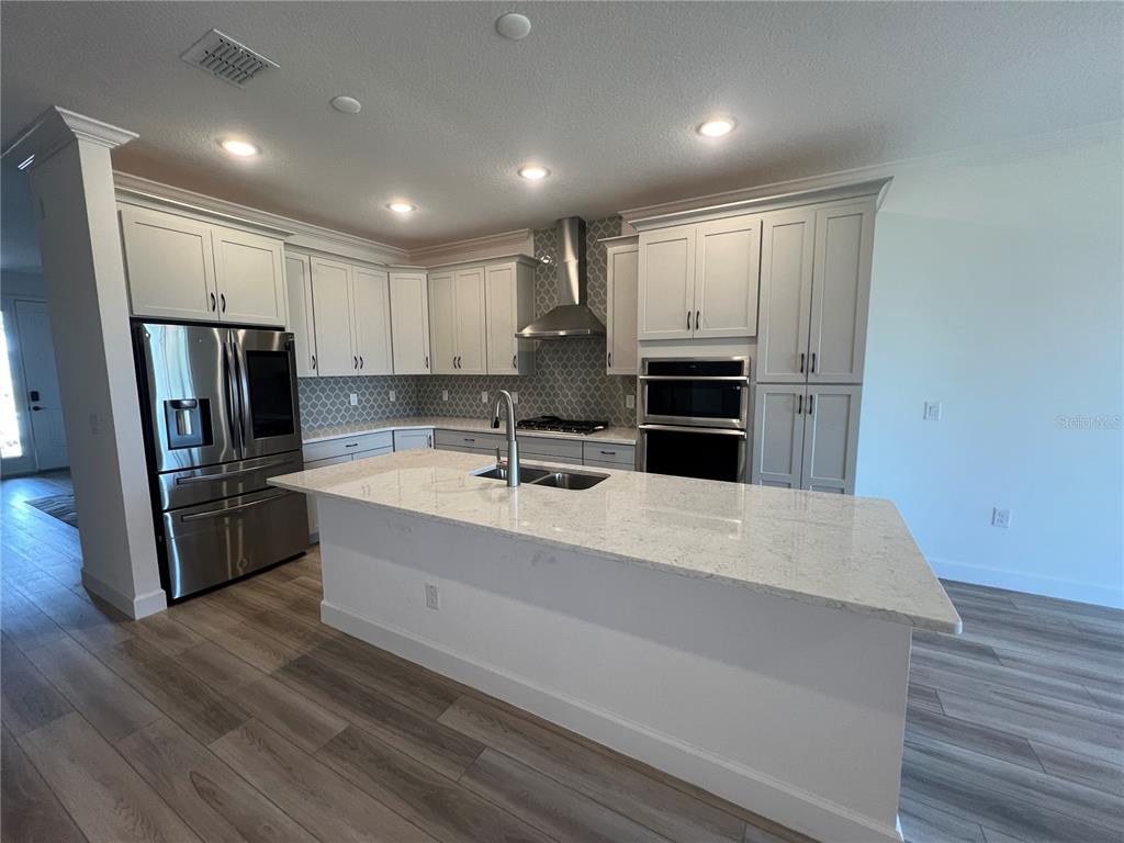 A modern kitchen features white cabinetry, stainless steel appliances, a large island, and tile backsplash — 931 SIGNET DRIVE, APOLLO BEACH, FL