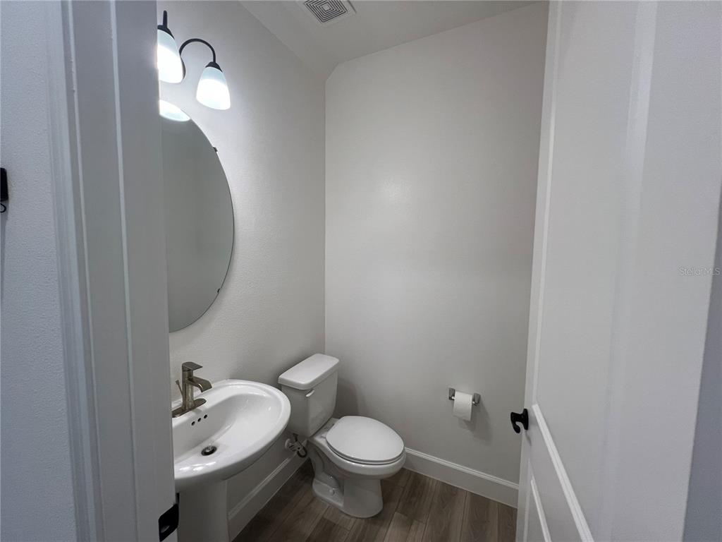 A small bathroom features a pedestal sink, a toilet, and a round wall mirror — 931 SIGNET DRIVE, APOLLO BEACH, FL