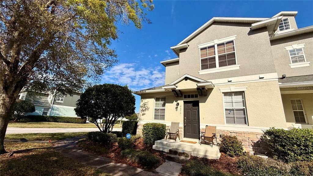 A two-story townhouse with a tan stucco exterior, stone accents, and a small front porch — 4670 CAPITAL BOULEVARD, ST CLOUD, FL
