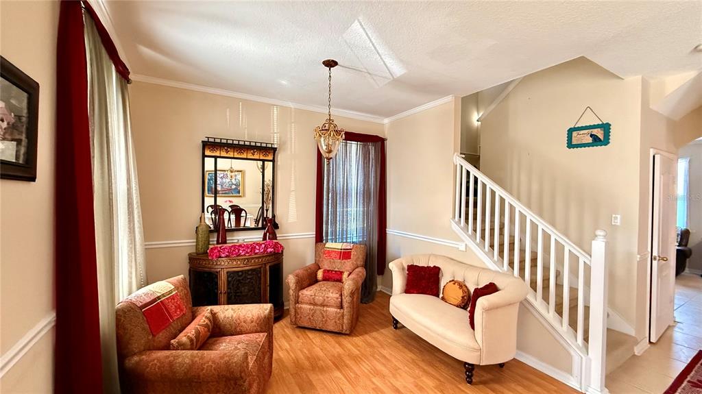 A living room features a staircase, two patterned armchairs, a beige sofa, and a mirror — 4670 CAPITAL BOULEVARD, ST CLOUD, FL