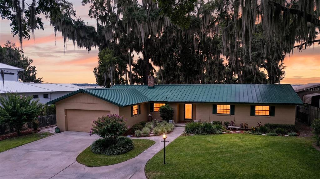 A single-story house with a green metal roof and a two-car garage at sunset — 13200 E HIGHWAY 25, OCKLAWAHA, FL