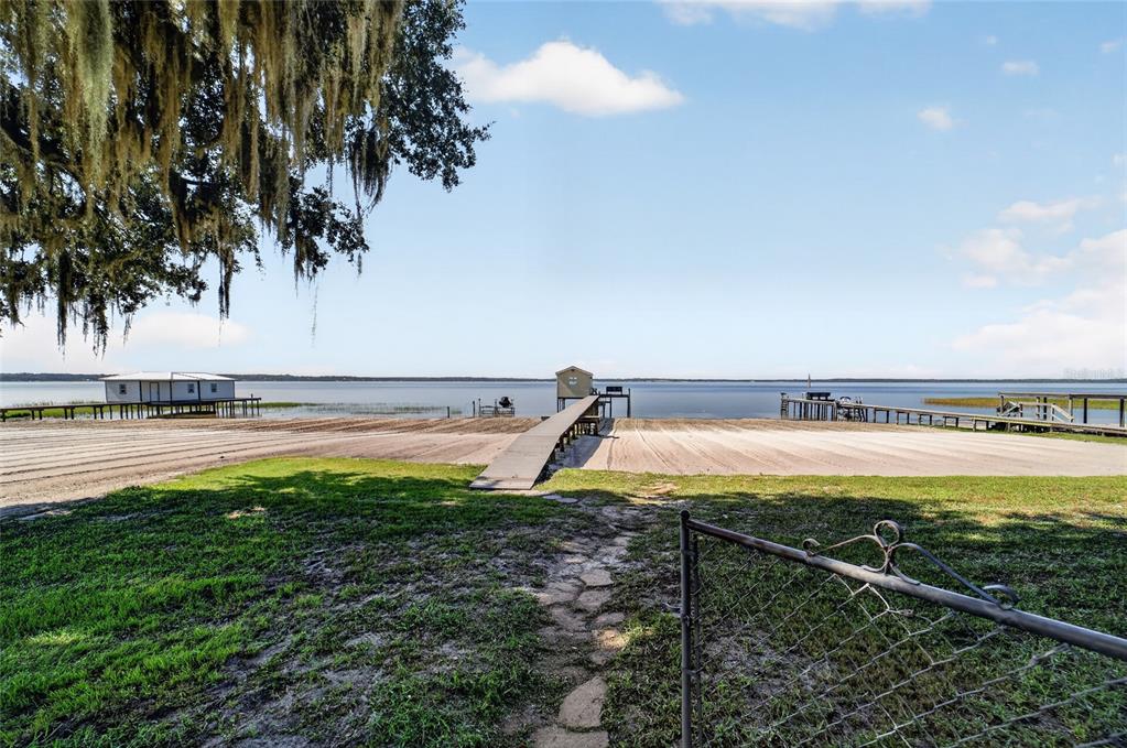 A grassy yard leads to a sandy beach and a wooden dock on a lake — 13200 E HIGHWAY 25, OCKLAWAHA, FL