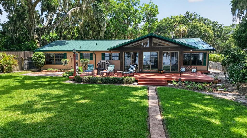 A single-story house with a green metal roof and a wooden deck overlooking a lawn — 13200 E HIGHWAY 25, OCKLAWAHA, FL