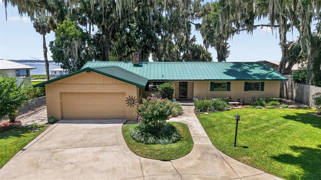 A single-story house with a green metal roof, tan siding, and an attached garage — 13200 E HIGHWAY 25, OCKLAWAHA, FL