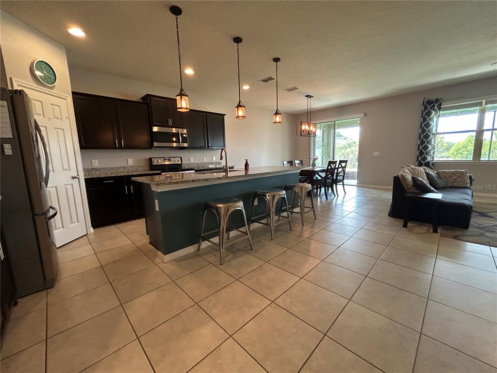 A kitchen with dark cabinets, a granite island with bar stools, and tile flooring — 3949 BAJA DRIVE, ST CLOUD, FL