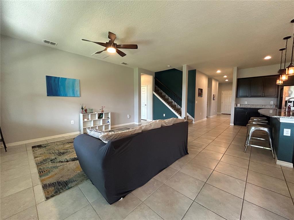 A living room with tile flooring, a gray sofa, and an open kitchen with dark cabinets — 3949 BAJA DRIVE, ST CLOUD, FL