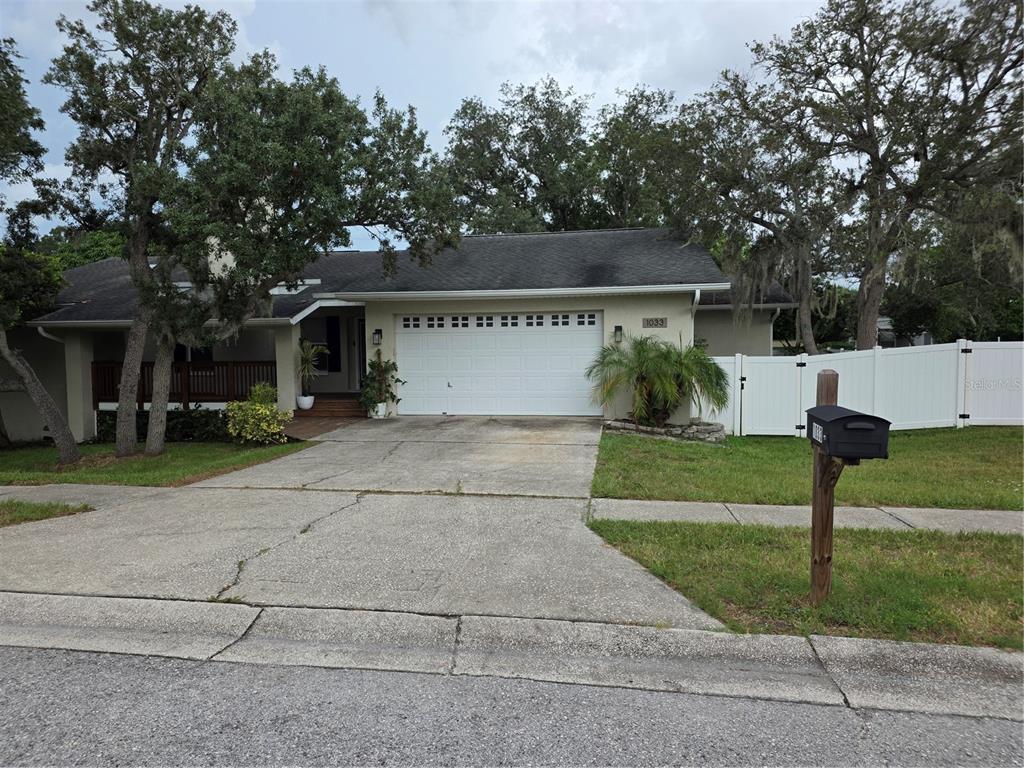 A single-story house with a white garage door, a concrete driveway, and a white fence — 1033 ROSETREE LANE, TARPON SPRINGS, FL