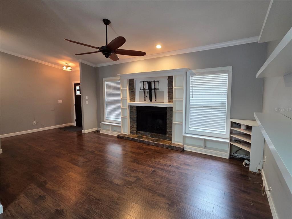 A living room features dark wood flooring, a stone fireplace with built-in shelving, and a ceiling fan — 1033 ROSETREE LANE, TARPON SPRINGS, FL