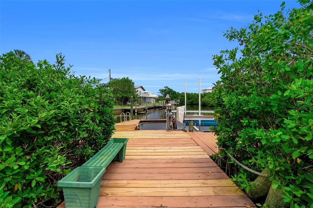 A wooden dock extends into a canal between lush green bushes and a boat lift — 332 SHORE DRIVE, ELLENTON, FL