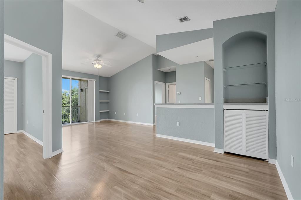 An open living area features light wood-look flooring, vaulted ceilings, a ceiling fan, and built-in shelving — 1150 LAKE SHADOW CIRCLE UNIT 3305, MAITLAND, FL