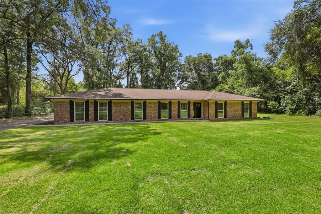 A single-story brick ranch house with black shutters sits on a large, grassy lawn — 226 SW 80TH BOULEVARD, GAINESVILLE, FL