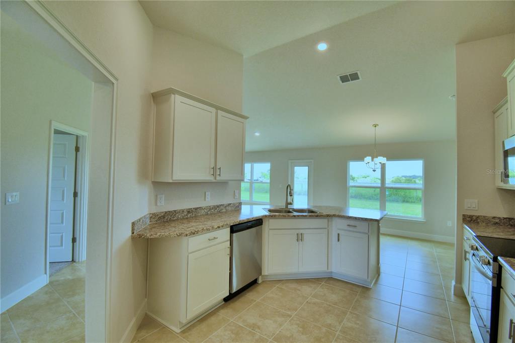 A kitchen with white cabinets, granite countertops, stainless steel appliances, and tile flooring — 4433 JUNEBERRY DRIVE, AUBURNDALE, FL