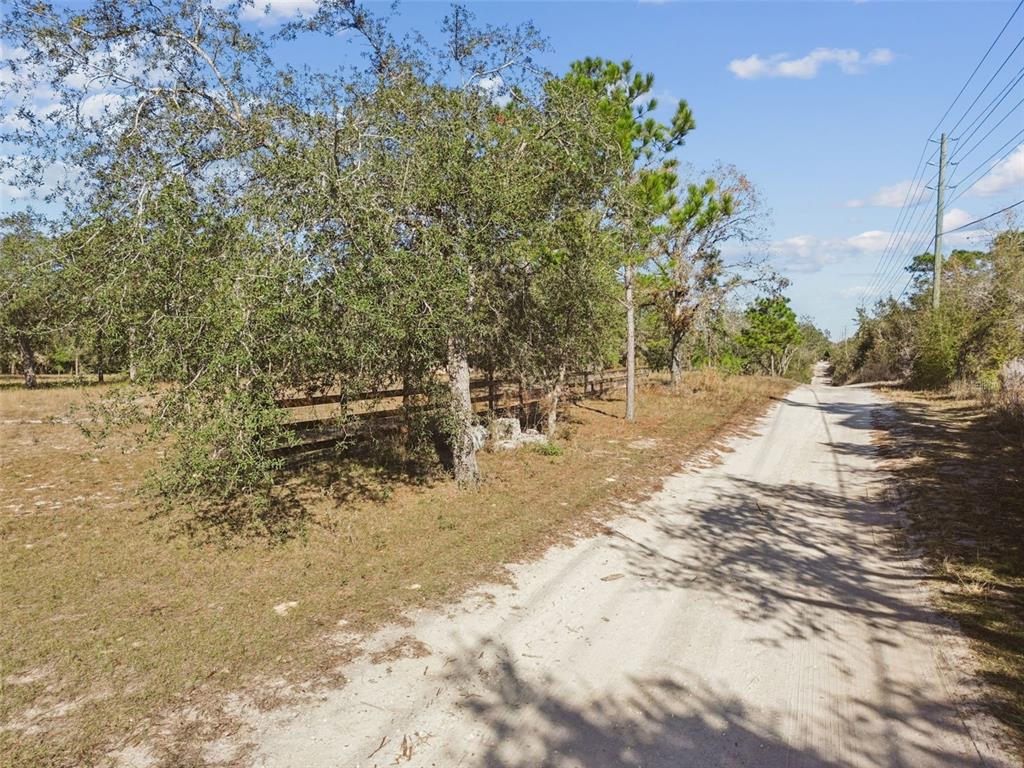 A dirt road runs alongside a wooden fence and trees under a clear blue sky — 14459 COYOTE ROAD, HUDSON, FL