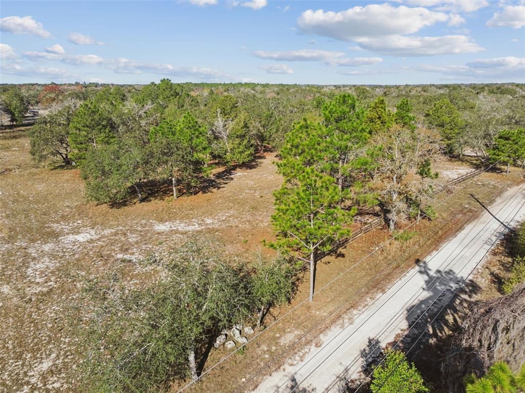 An aerial view shows a dirt road bordering a grassy lot with scattered trees — 14459 COYOTE ROAD, HUDSON, FL