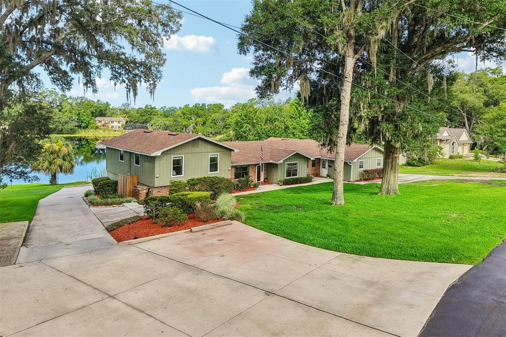 A green house with a brown roof sits on a grassy lot beside a lake — 1460 GROVE STREET, EUSTIS, FL