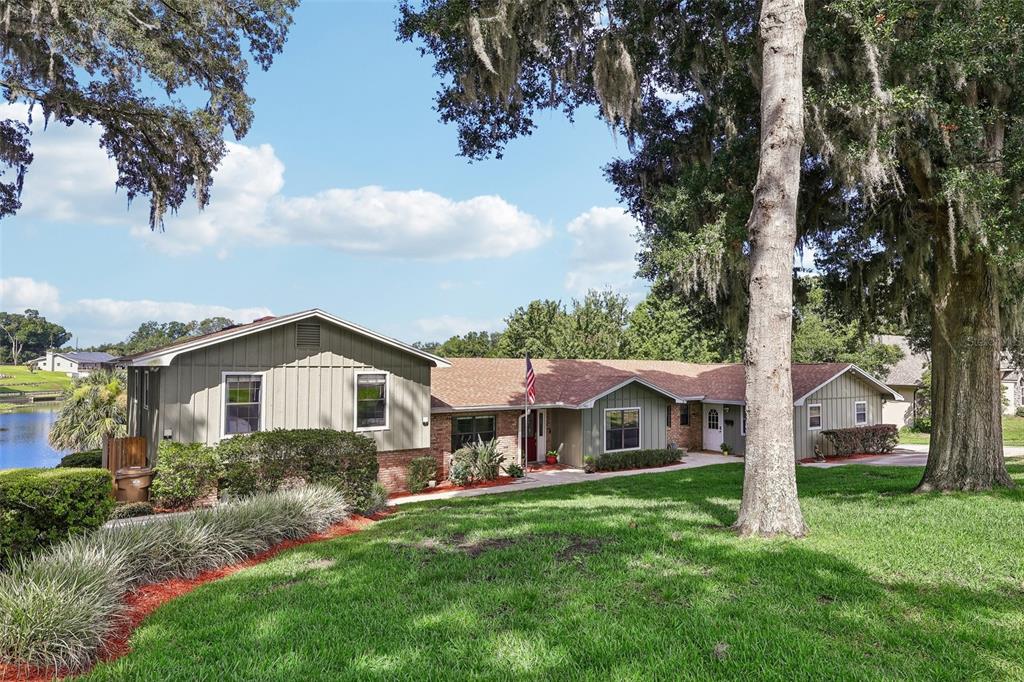 A single-story house with olive green siding and a brick base sits on a lawn — 1460 GROVE STREET, EUSTIS, FL
