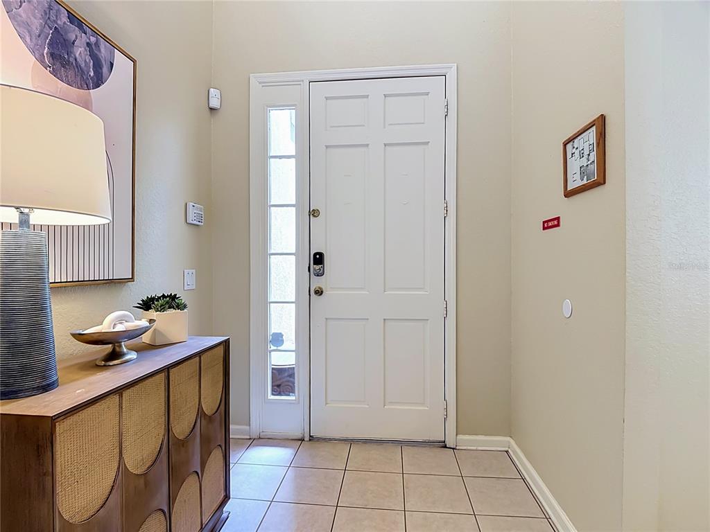 An entryway features a white door with a sidelight, tiled flooring, and a wooden console table — 7742 COMROW ST, KISSIMMEE, FL