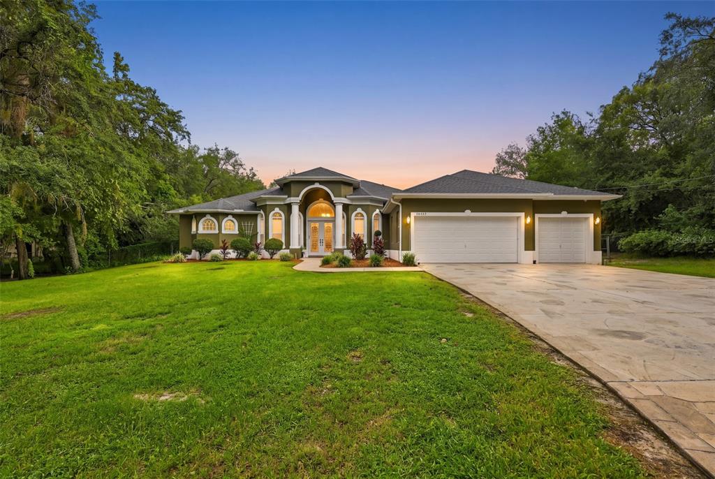 A single-story house with an olive green exterior, white trim, and a three-car garage — 16547 CROSSANDRA LANE, SPRING HILL, FL
