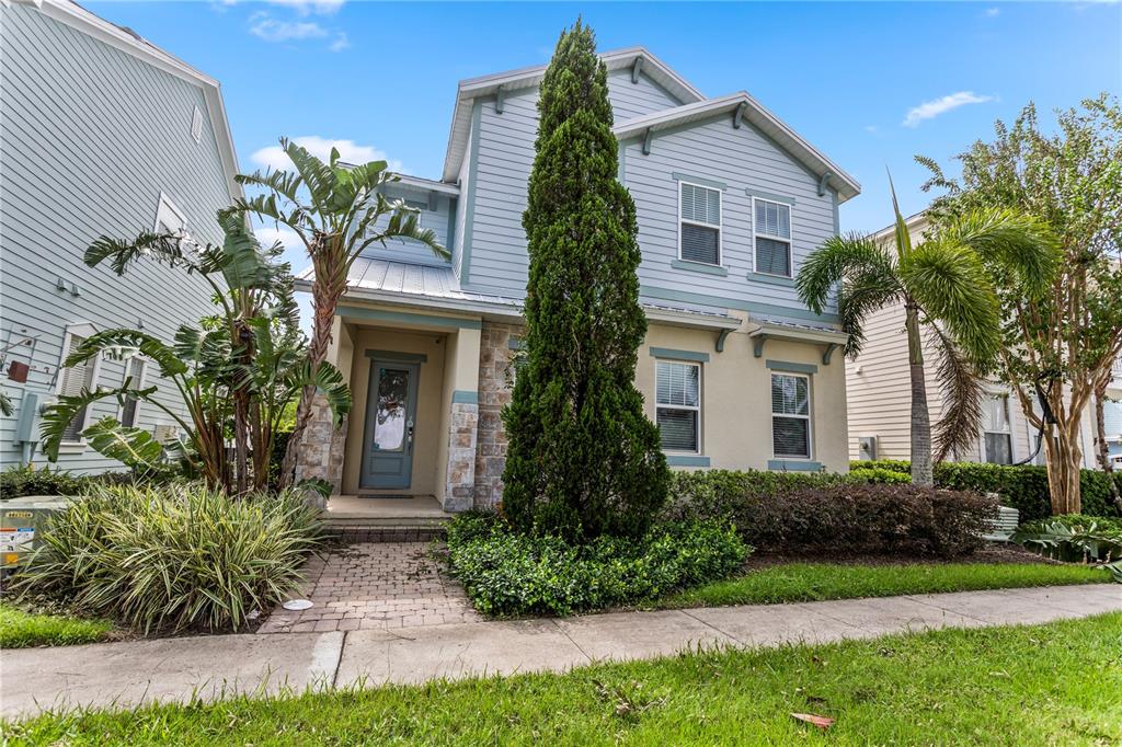 A two-story house with light blue siding, stone accents, and a tall central evergreen tree — 1407 FAIRVIEW CIRCLE, REUNION, FL