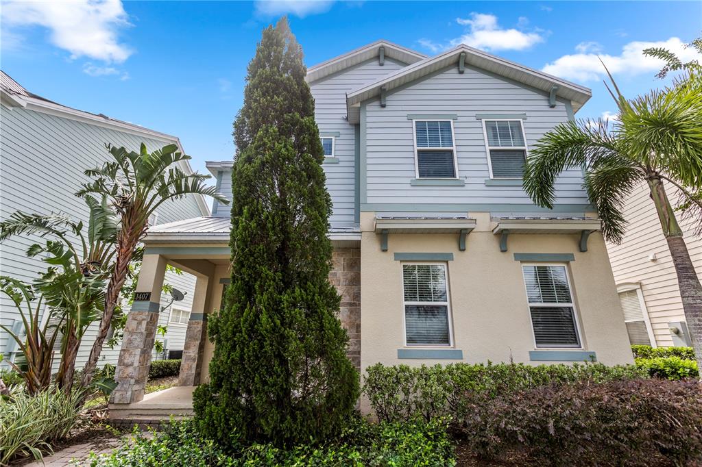 A two-story house with light blue siding, stone accents, and a tall evergreen tree — 1407 FAIRVIEW CIRCLE, REUNION, FL
