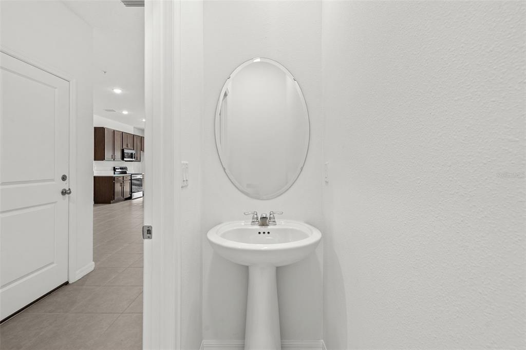 A white bathroom vanity with an oval mirror sits beside a doorway leading to a kitchen — 4899 WINDING RIVER ROAD, ORLANDO, FL