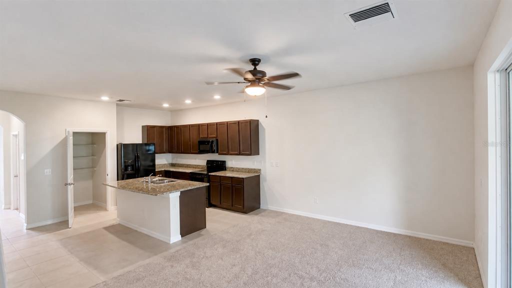 An open-concept kitchen features dark wood cabinets, granite countertops, an island, and carpeted flooring — 32935 KALOKO ROAD, WESLEY CHAPEL, FL