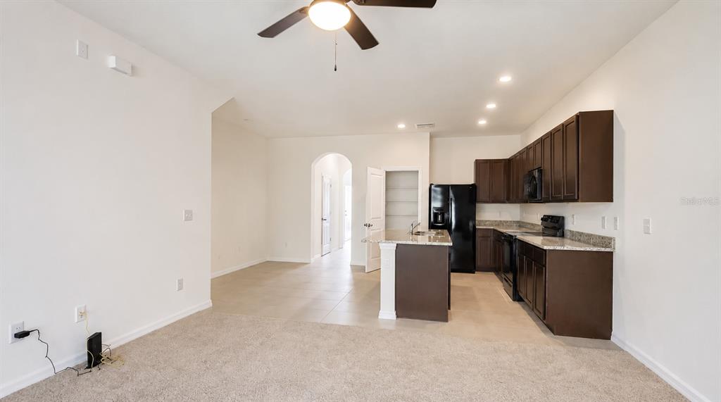 A kitchen with dark cabinets and an island opens into a carpeted living area — 32935 KALOKO ROAD, WESLEY CHAPEL, FL