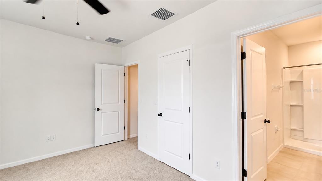 A bedroom with beige carpet, white walls, three doors, and an attached bathroom — 32935 KALOKO ROAD, WESLEY CHAPEL, FL