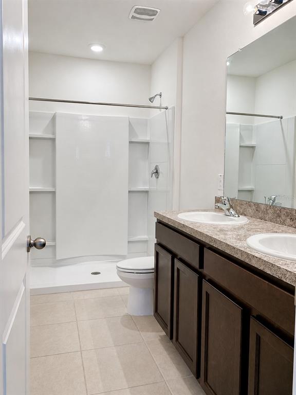 A bathroom features a walk-in shower, a toilet, and a double-sink vanity with dark cabinets — 32935 KALOKO ROAD, WESLEY CHAPEL, FL