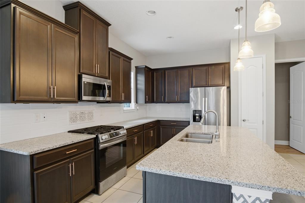 A kitchen with dark wood cabinets, granite countertops, stainless steel appliances, and a central island — 5027 E FOUNTAINWOOD DRIVE, ST CLOUD, FL