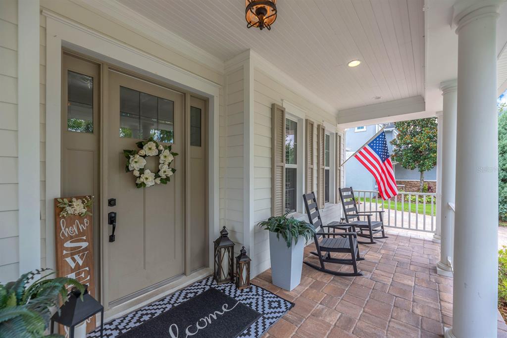 A covered front porch features a neutral door with a wreath, rocking chairs, and an American flag — 5202 ALAFIA FALLS DRIVE, LITHIA, FL