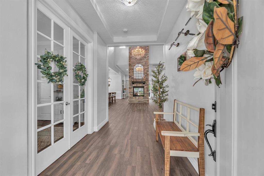 A bright entryway features wood-look flooring, French doors, and a stone fireplace in the distance — 5202 ALAFIA FALLS DRIVE, LITHIA, FL