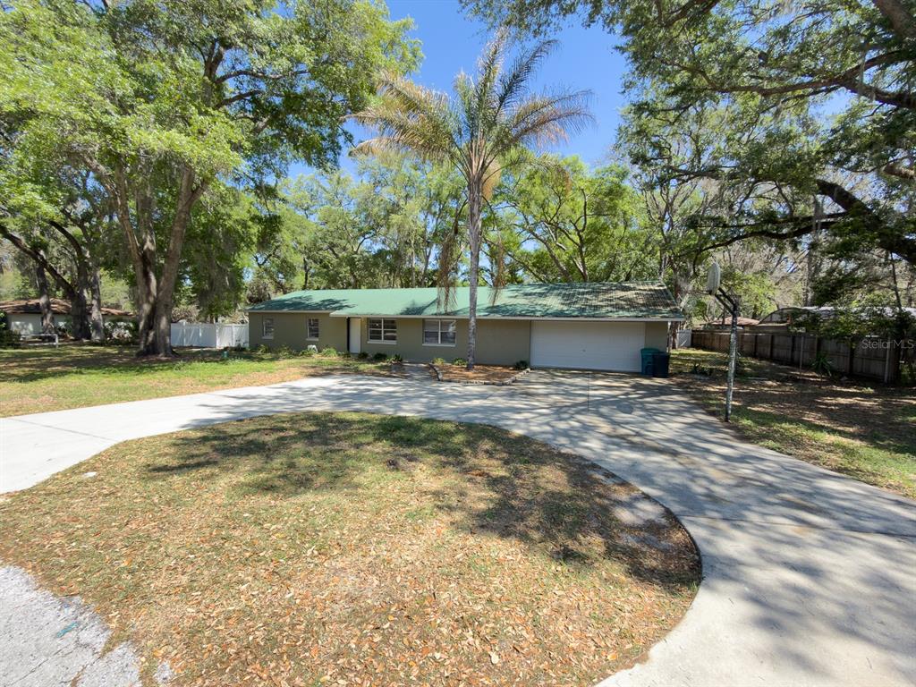 A single-story house with a green metal roof, a two-car garage, and a circular driveway — 207 MANDARIN LN, FRUITLAND PARK, FL